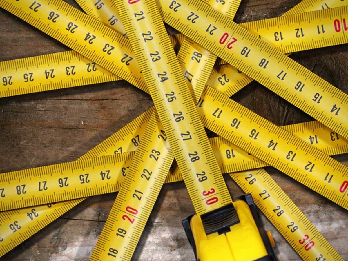 Yellow measuring tapes are sprawled across a wooden surface, with one tape prominently positioned, indicating various length measurements amidst a cluttered arrangement.