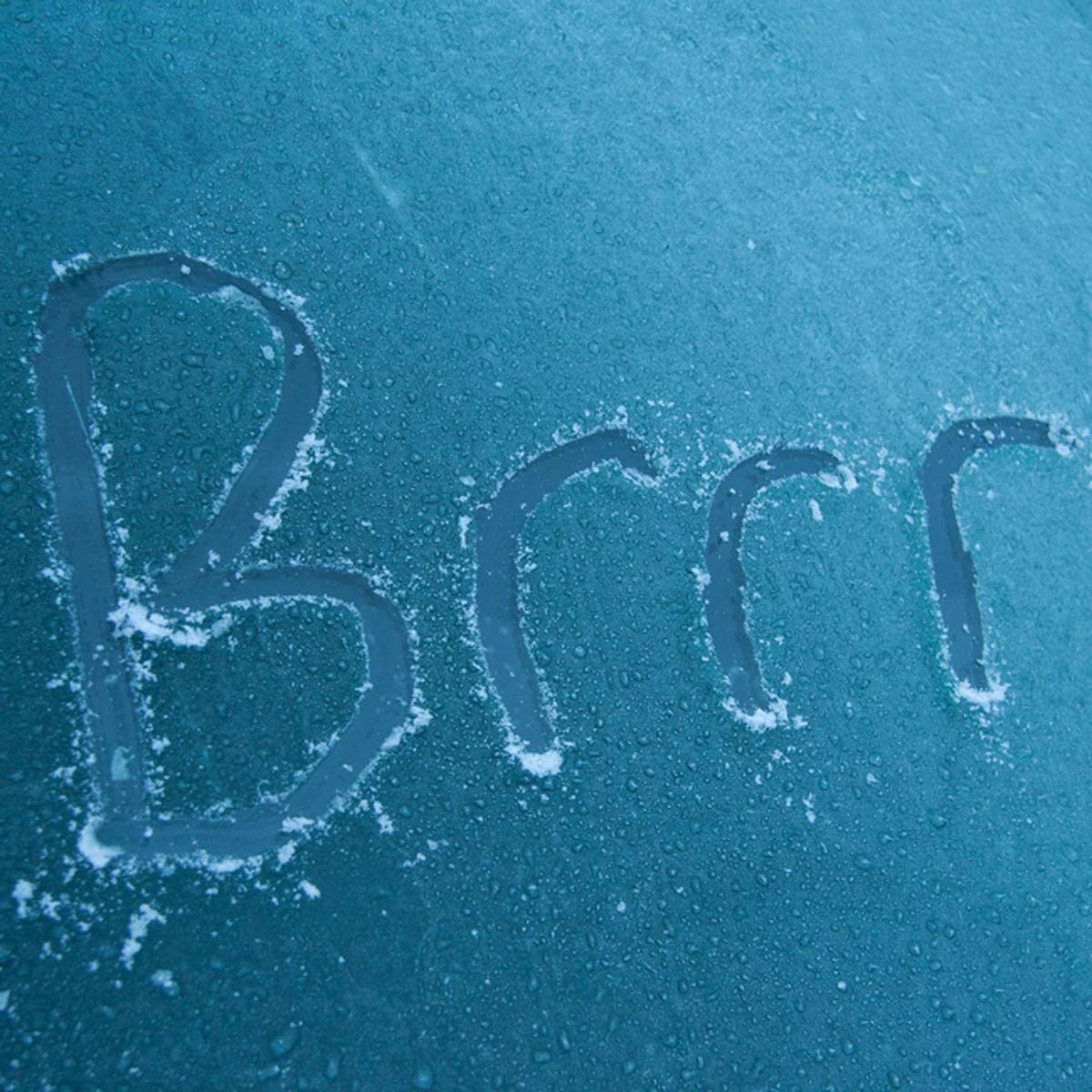 A frosty surface displays the word "Brrr" etched into it, surrounded by small droplets of water and a light dusting of frost.