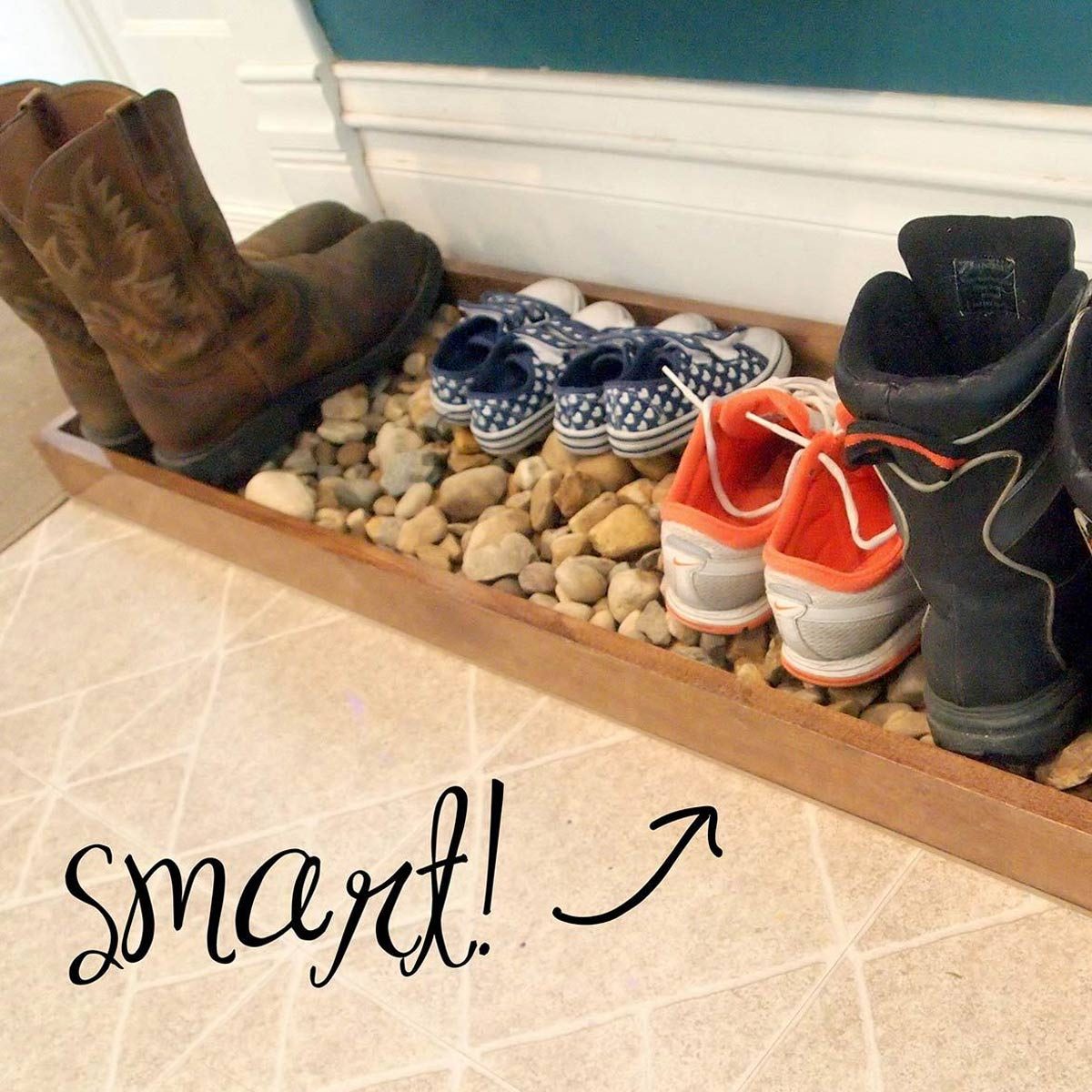 A wooden shoe rack holds various footwear, including boots and sneakers, surrounded by small stones, with a cheerful message saying "smart!" nearby.