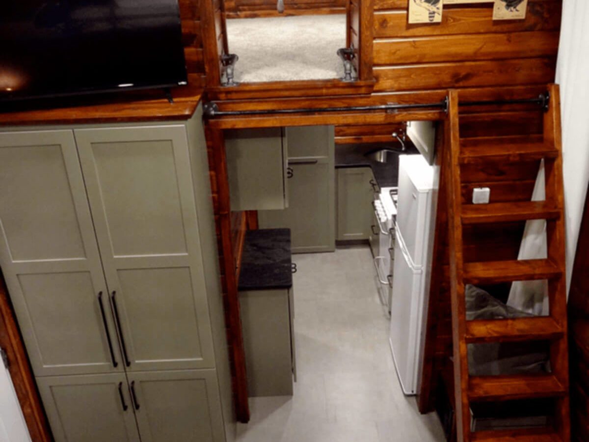 A kitchen features fitted cabinets and appliances, while a staircase leads to an upper loft area, all within a rustic, wooden interior.