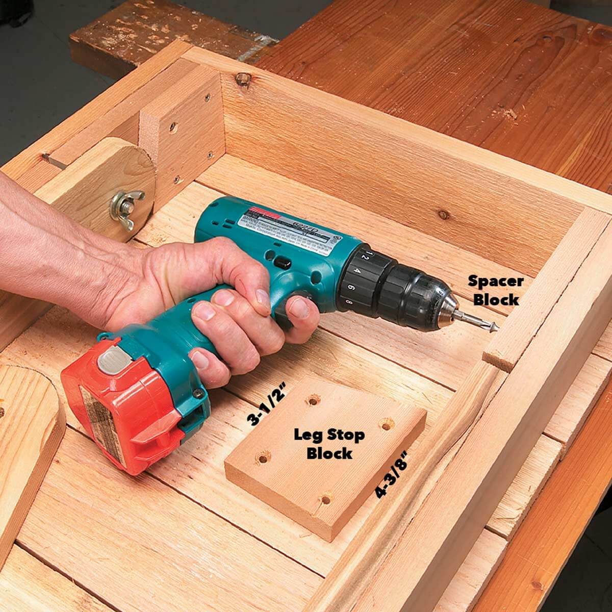 A hand grips a cordless drill, driving a screw into wooden blocks labeled "Spacer Block" and "Leg Stop Block" on a work surface.