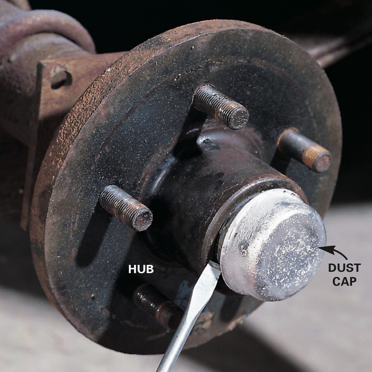 A metal hub with bolts is being worked on, as a tool pries off a dust cap in a dimly lit, mechanical setting.