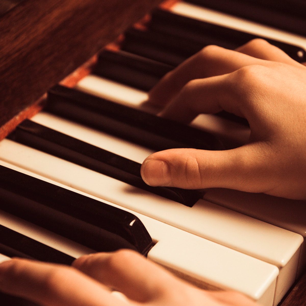 A pair of hands presses piano keys, producing music. The scene focuses on the keyboard's black and white keys, with a wooden surface in the background.