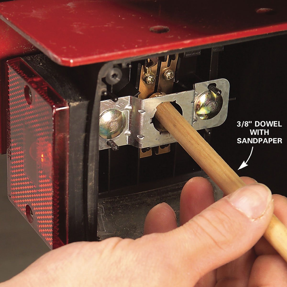A dowel is inserted into a metal bracket for sanding, with a hand positioned for control. The context suggests equipment maintenance.