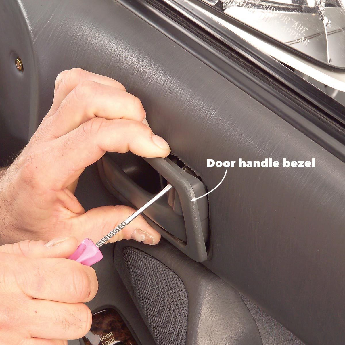 A hand uses a small tool to remove a door handle bezel from a car interior, surrounded by textured gray material and a partially visible door lock.