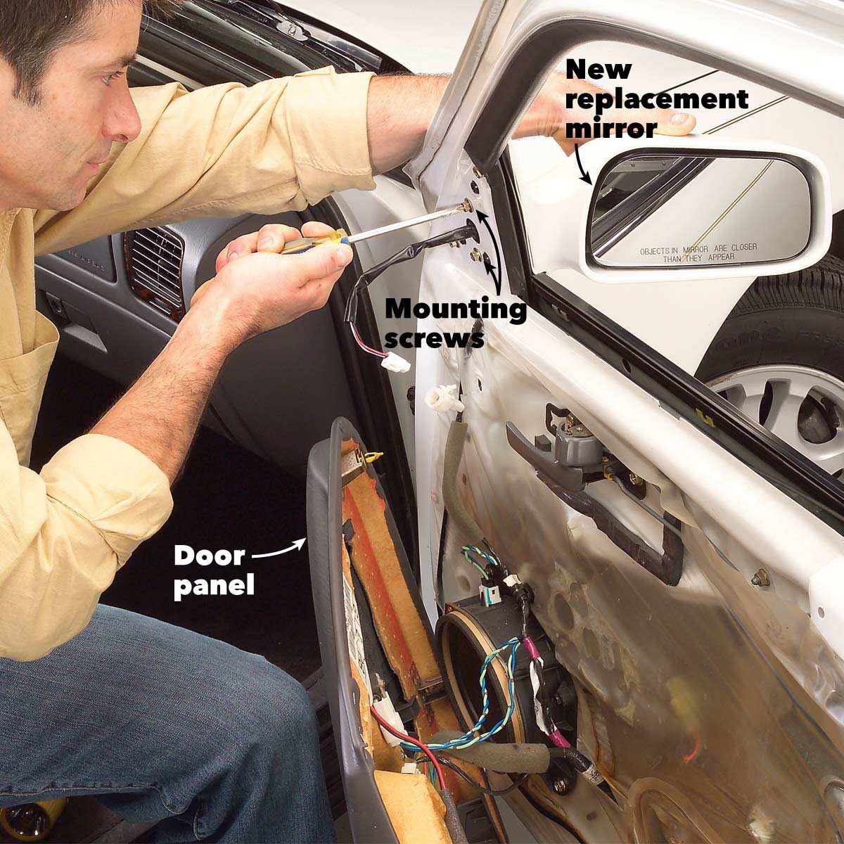 A man installs a new mirror inside a car door, using a screwdriver on mounting screws, with the door panel partially removed.