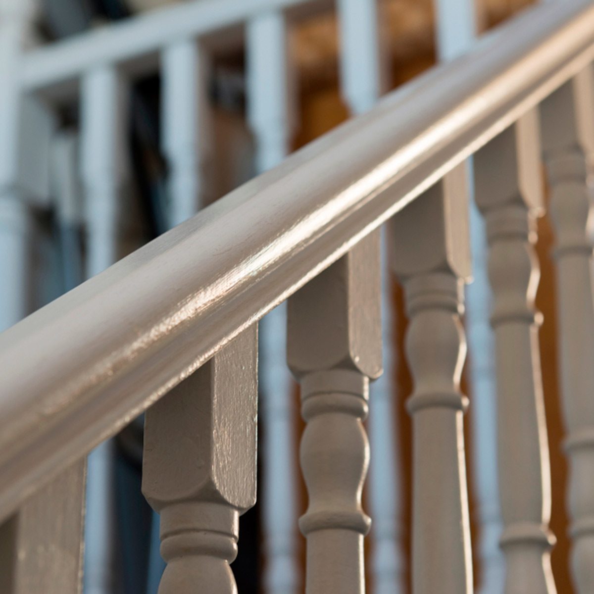 A polished handrail slopes downwards, supported by decorative spindles, set against a softly lit indoor environment.