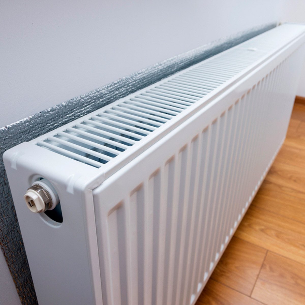 A white panel radiator is mounted on a wall, providing heat in a room with wooden flooring and a light-colored wall.