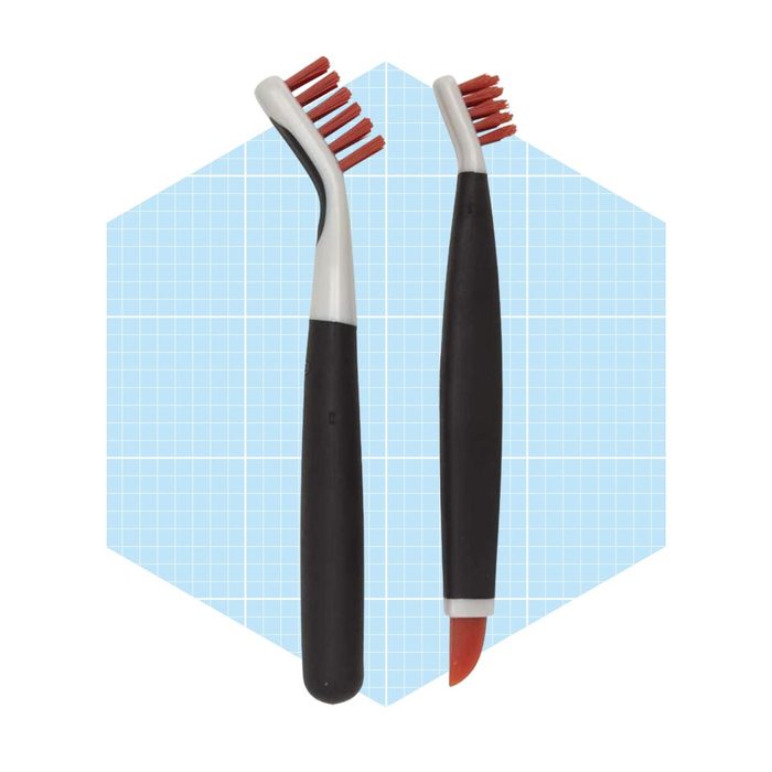 Two toothbrushes with red bristles are positioned side by side against a light blue grid background, emphasizing their design and usage for cleaning.