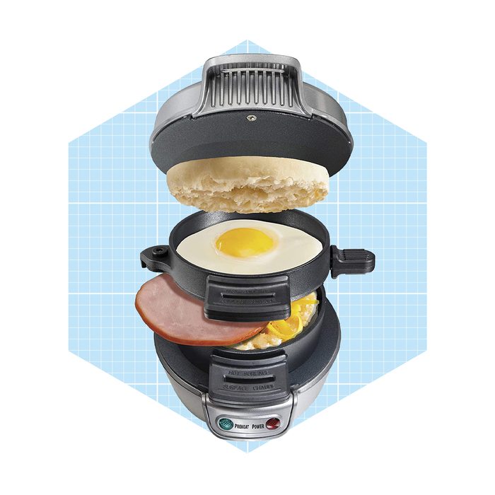 A stacked breakfast sandwich maker with an egg, ham, and a muffin partially assembled, set against a simple grid background.