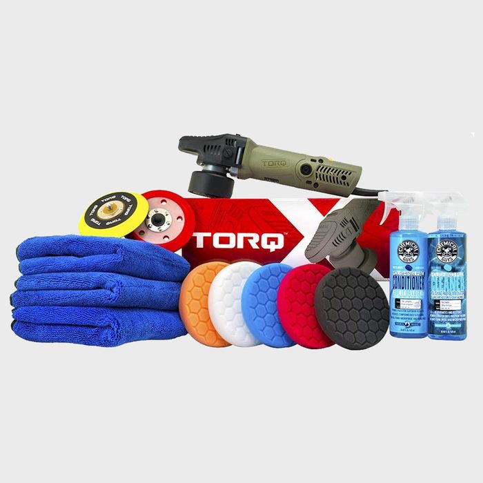 A polisher rests on a red brand box, surrounded by various colored foam pads, blue microfiber towels, and cleaning products, ready for detailing tasks.
