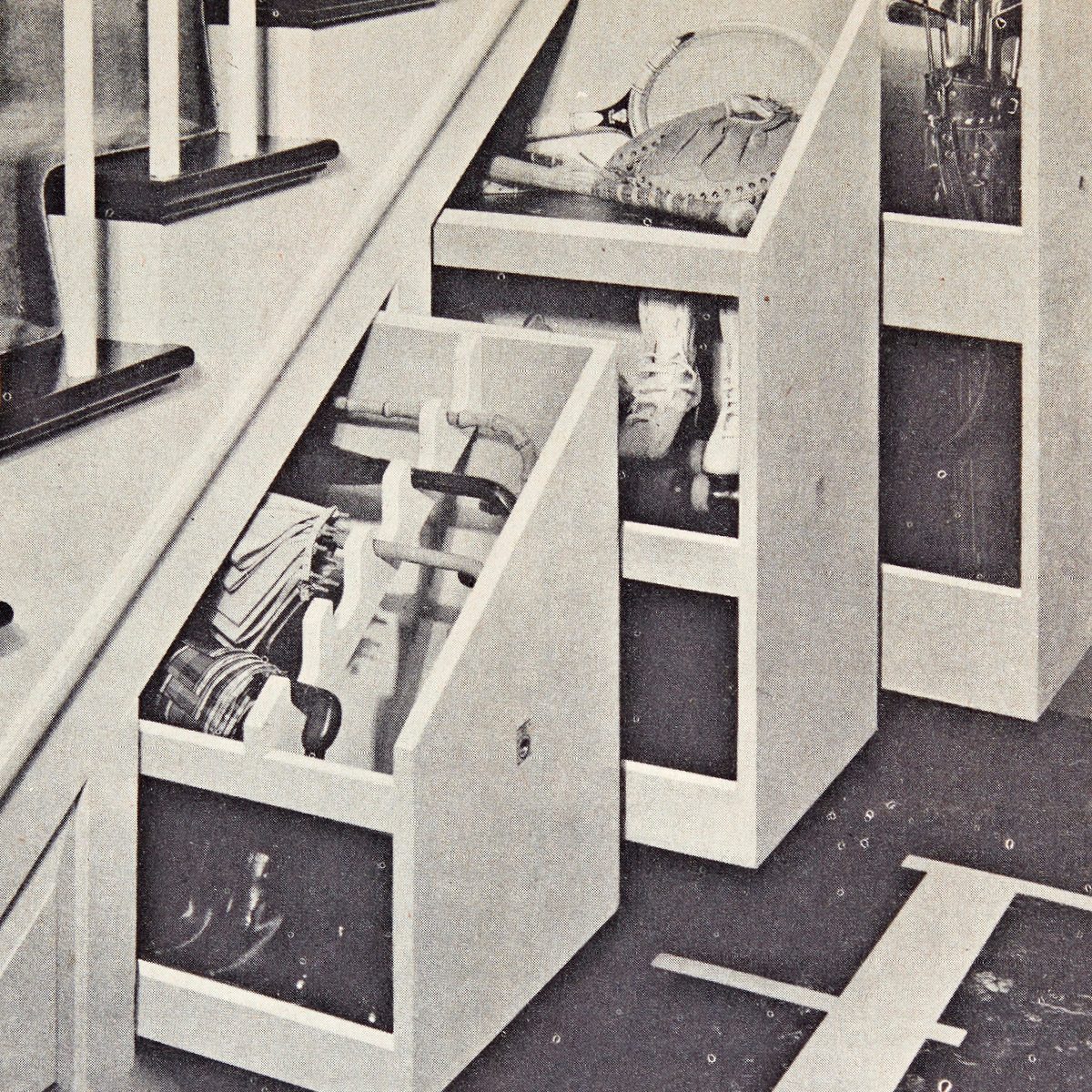 Storage compartments display various sports equipment, umbrellas, and footwear, organized neatly against a wall near stairs in a functional indoor environment.