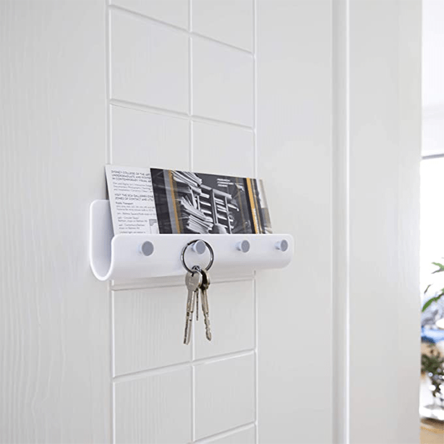 A white wall-mounted holder displays a card and securely holds keys, enhancing organization in a bright, minimalist indoor space.
