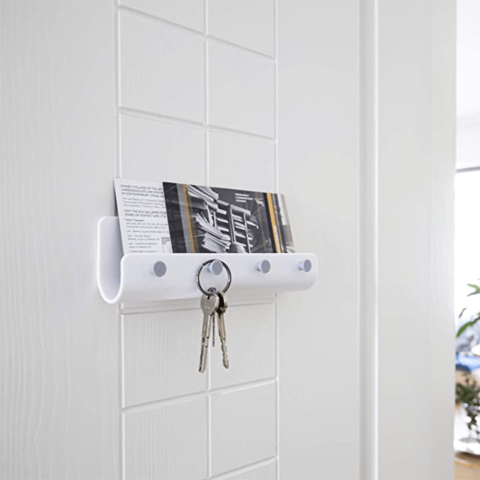 A white wall-mounted holder displays a card and securely holds keys, enhancing organization in a bright, minimalist indoor space.
