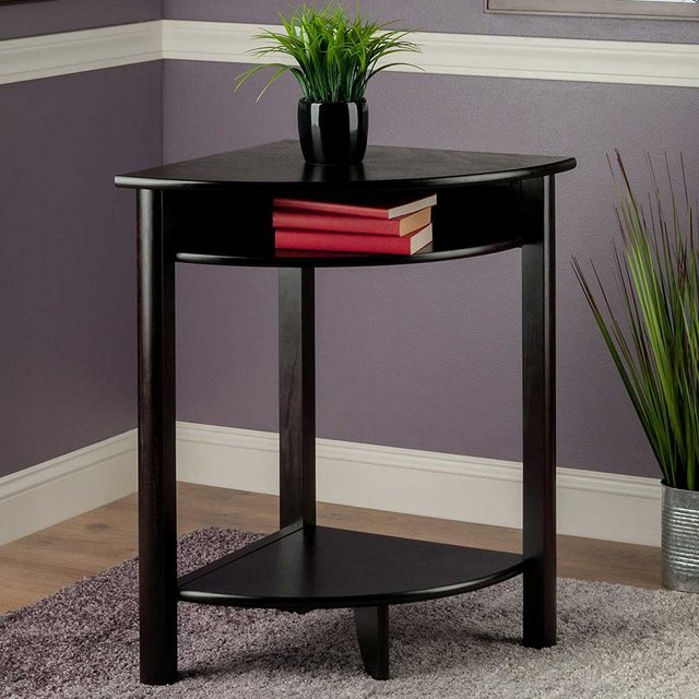 A black corner table holds red books and a small plant, situated in a room with purple walls, wooden floor, and a textured rug.