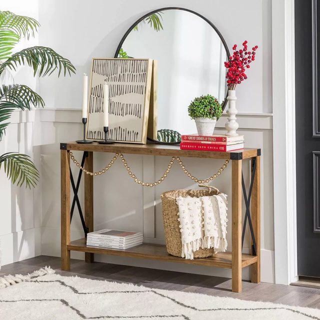A wooden console table displays decorative items, including a mirror, plants, and books, next to a black door, surrounded by light walls and a soft rug.