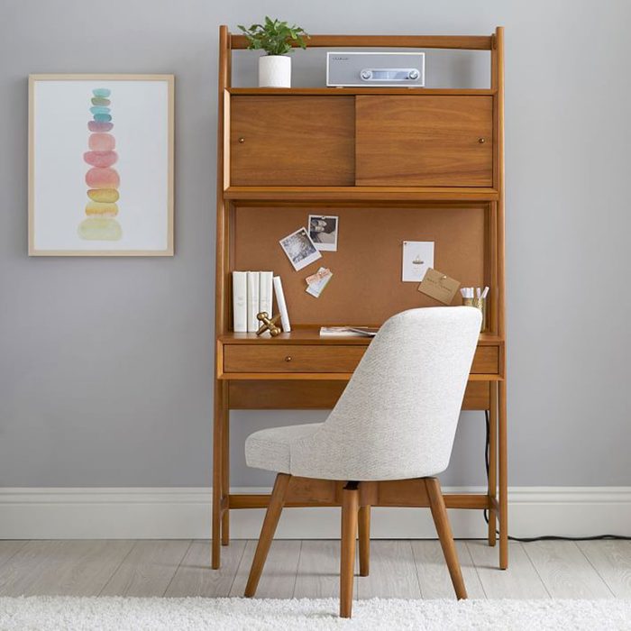 A wooden desk with a chair is arranged against a gray wall, featuring a potted plant, radio, and framed artwork above it, creating a cozy workspace.
