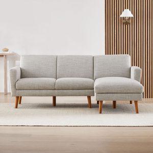 A light gray sofa with wooden legs sits on a textured rug, facing a wooden slatted wall and a small side table with decor.