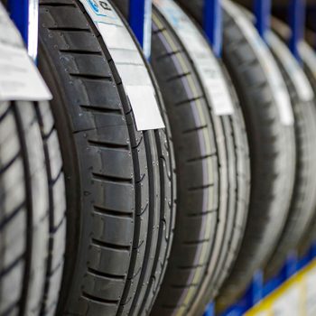 Tires are displayed vertically on blue racks, showcasing their tread patterns and labels in a well-lit storage area.