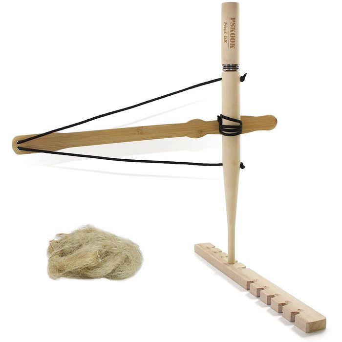 A spinning tool stands upright on a base, with a soft fiber nest nearby. The tool is designed for creating yarn or thread.