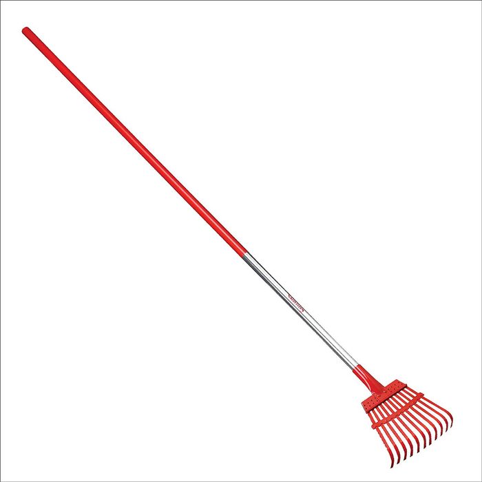 A long-handled rake with a red plastic handle and metal head rests vertically against a plain white background, ready for use in gardening or yard work.