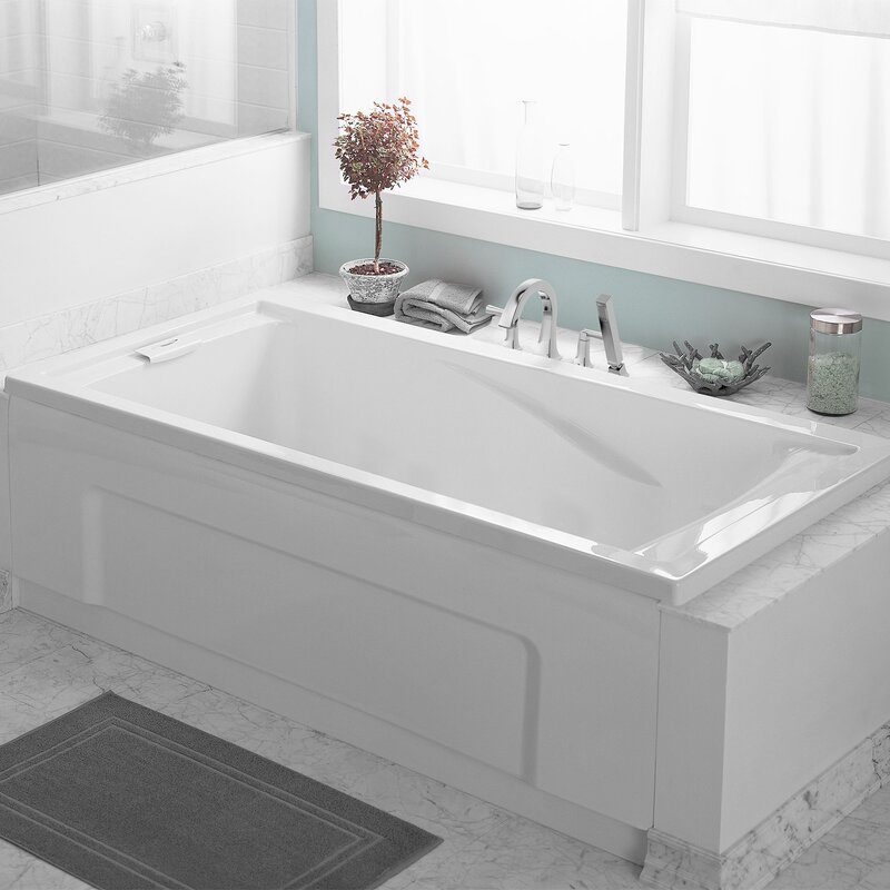 A white bathtub is situated on a marble floor, surrounded by a light green wall, with a small plant, towels, and decorative items nearby.