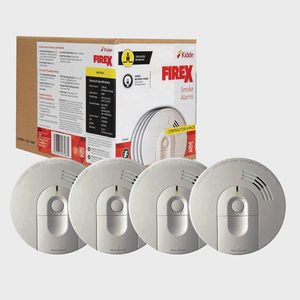 Four smoke alarms are displayed in front of a cardboard packaging. The alarms are round with a central button and indicator light, suggesting safety equipment for fire detection.