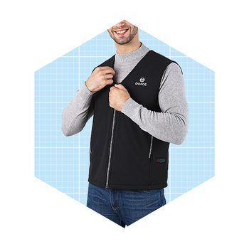 A man is zipping up a black vest over a gray sweater, smiling against a light blue grid background.