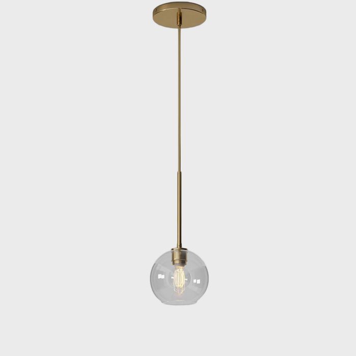 A round glass pendant light hangs from a golden fixture, illuminating a plain white background. The light bulb inside is visible and glowing softly.