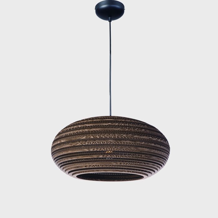 A round, striped pendant light hangs from a ceiling, illuminating its surroundings with a unique design and a warm ambiance against a neutral background.