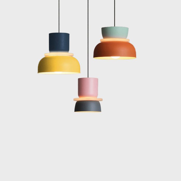 Three colorful pendant lamps hang from a ceiling, illuminating a minimalistic, neutral background. Each lamp features varying shapes and sizes, enhancing visual interest.