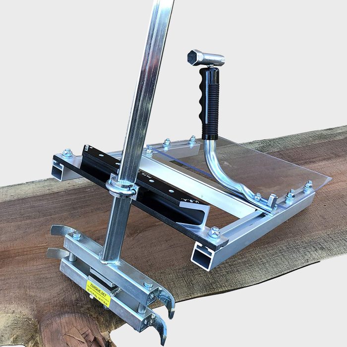 A log milling attachment rests on a wide wooden slab, holding the log in place as it prepares for cutting, surrounded by a natural wood surface.