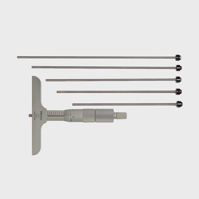 A micrometer gauge rests next to four metal probes, used for precise measurements, positioned on a neutral background, showcasing their streamlined design and functionality.