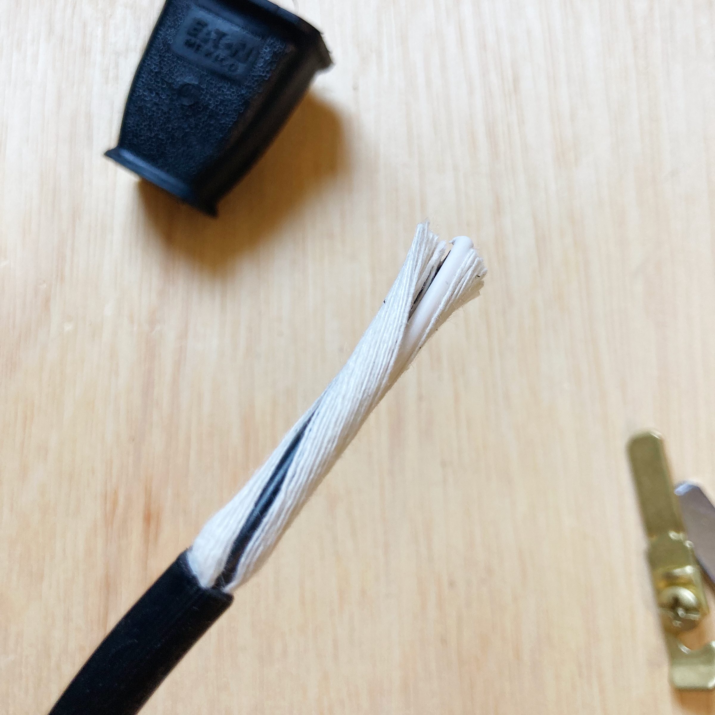 A stripped electrical wire with exposed inner strands lies on a wooden surface, beside a black plastic connector and a small metallic object.