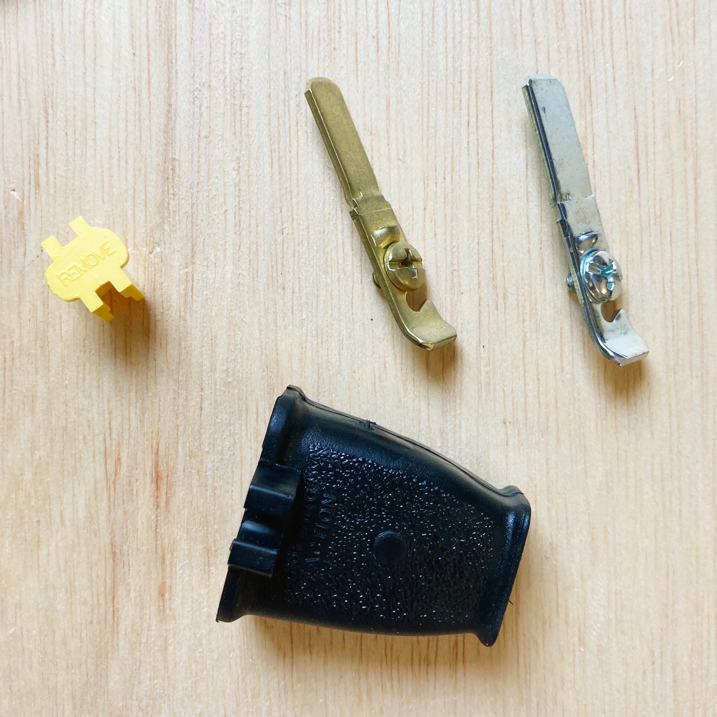 Three metallic clips and a black plastic piece arranged on a wooden surface, suggesting assembly or maintenance tools for an unspecified device.