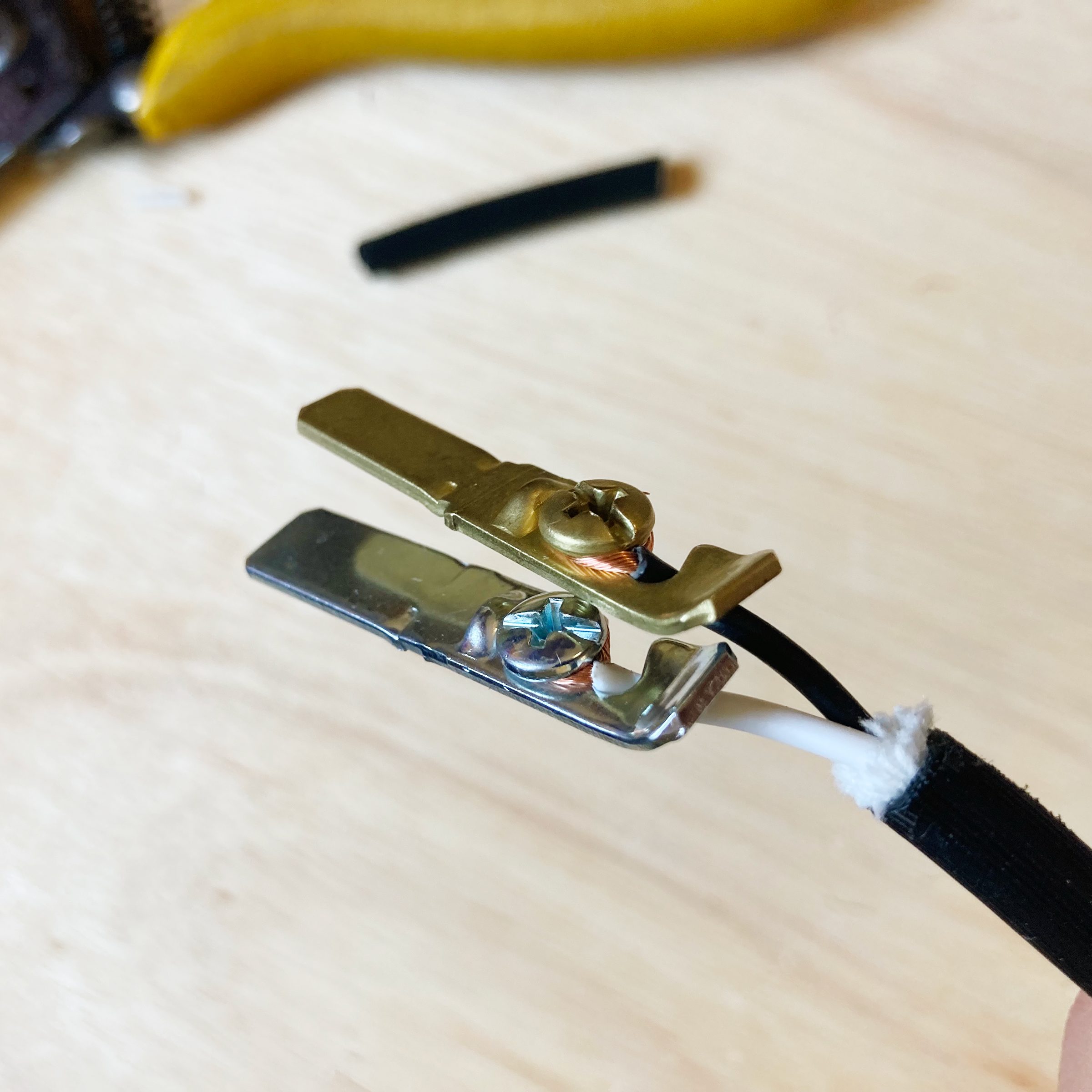 A connector clip is attached to a wire, securing it as part of an electrical assembly on a wooden surface, with tools visible in the background.