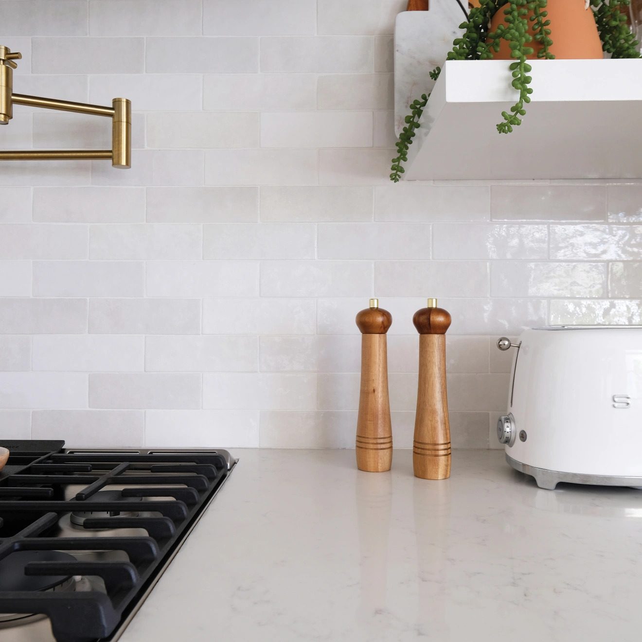Two wooden pepper mills stand on a white countertop beside a white kettle, set against a light tiled backsplash in a modern kitchen.