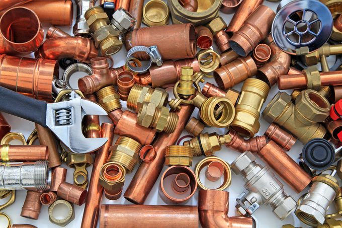 A wrench rests atop a chaotic assortment of copper and brass plumbing fittings, surrounded by various connectors and pipes, on a neutral background.