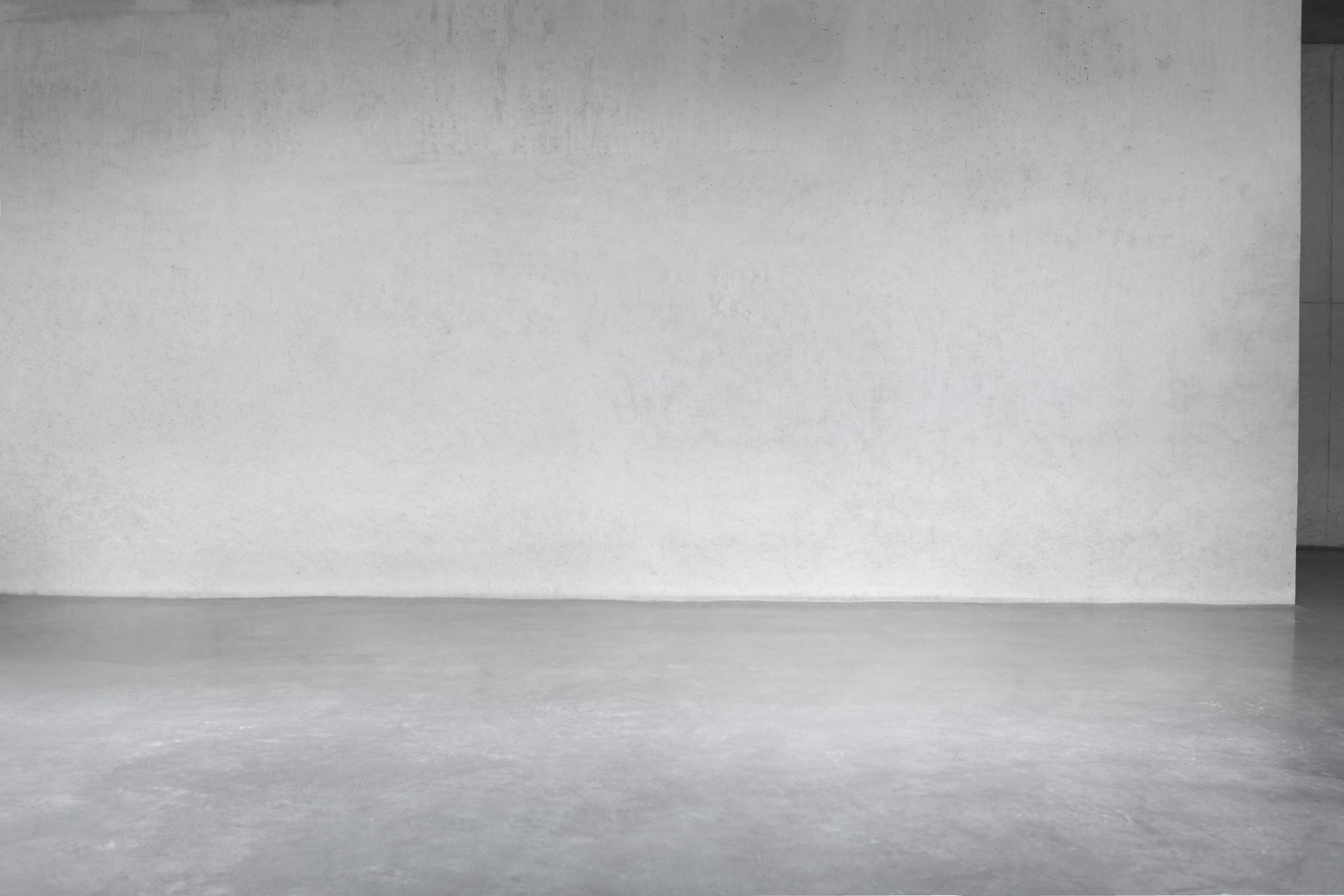 A smooth, light gray wall stands still, reflecting ambient light on a similarly colored floor in an empty, minimalistic space.