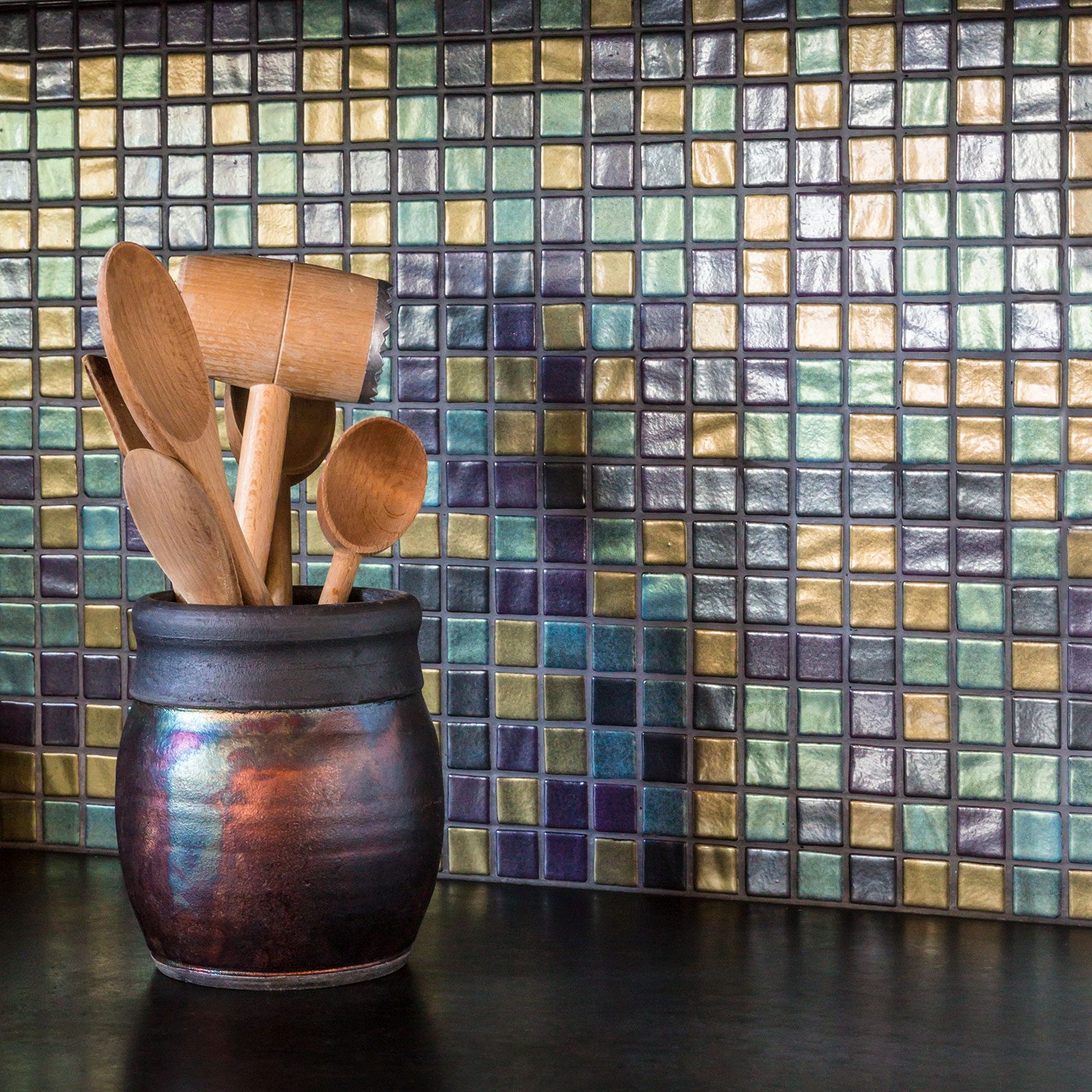 A ceramic pot holds various wooden cooking utensils, prominently displayed against a colorful mosaic tile background, creating a warm kitchen ambiance.