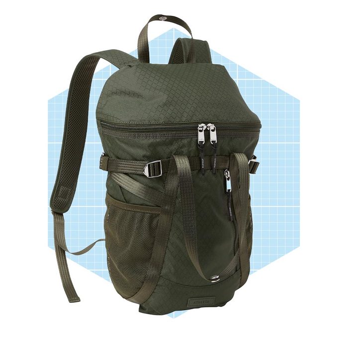 A green, textured backpack stands upright with dual zippers and side mesh pockets, set against a light blue geometric background.
