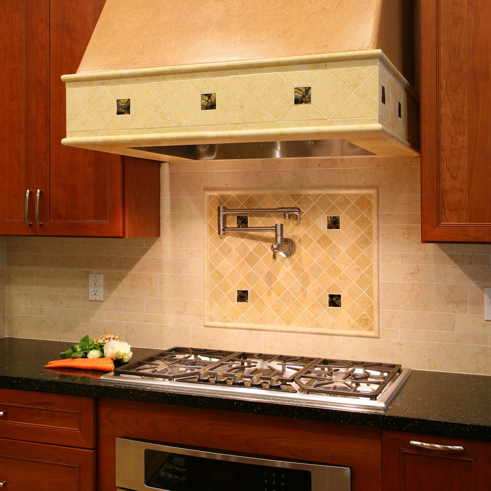 A modern kitchen features a gas stove under a decorative hood, with sleek cabinets, a tiled backsplash, and fresh vegetables on a granite countertop.