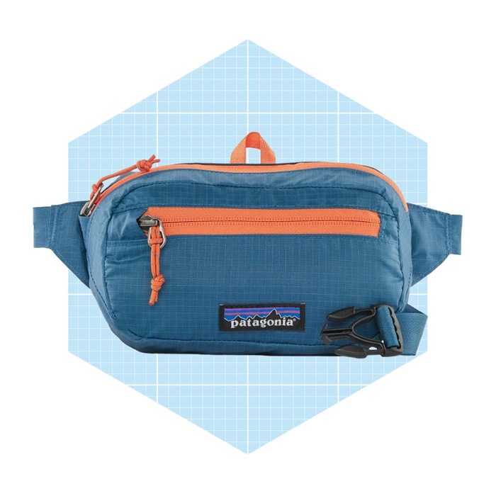 A blue fanny pack rests flat, featuring an orange zipper and adjustable strap, set against a light blue geometric background.