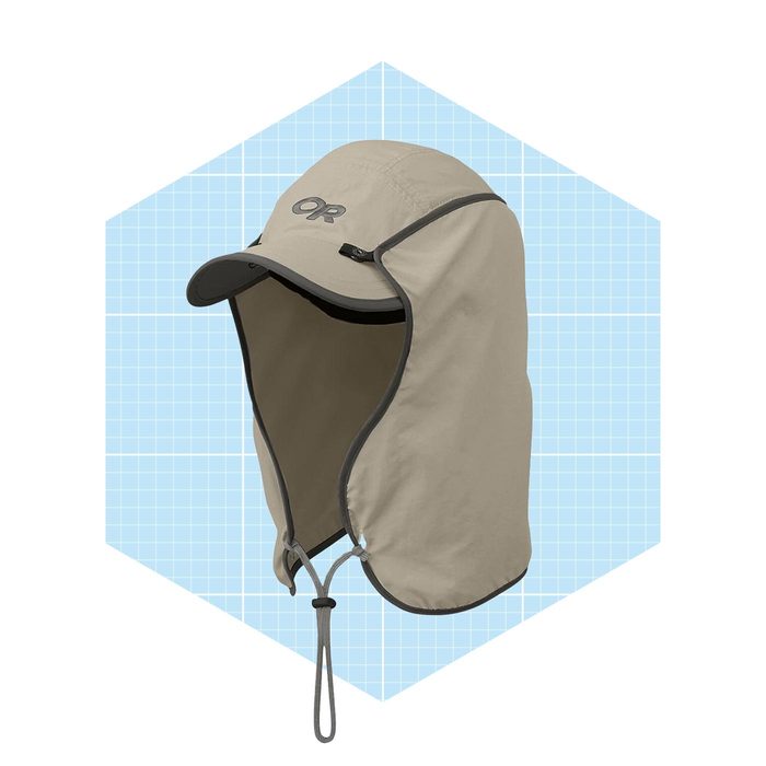 A beige sun hat with a wide brim and a neck cover hangs against a light blue, grid-patterned background, designed for sun protection.