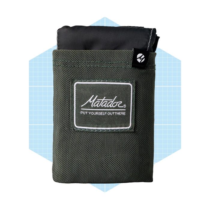 A dark green pack with a mesh exterior displays a logo and text, resting against a light blue geometric background.