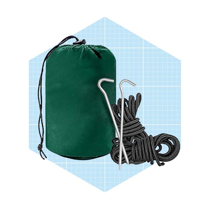 A green storage bag sits next to two metal stakes and bundles of black rope on a light blue grid background.