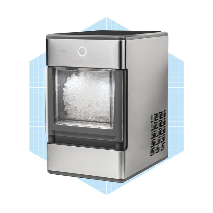 A stainless steel ice maker fills its transparent bin with ice cubes, placed against a light blue geometric background, suggesting a modern kitchen setting.