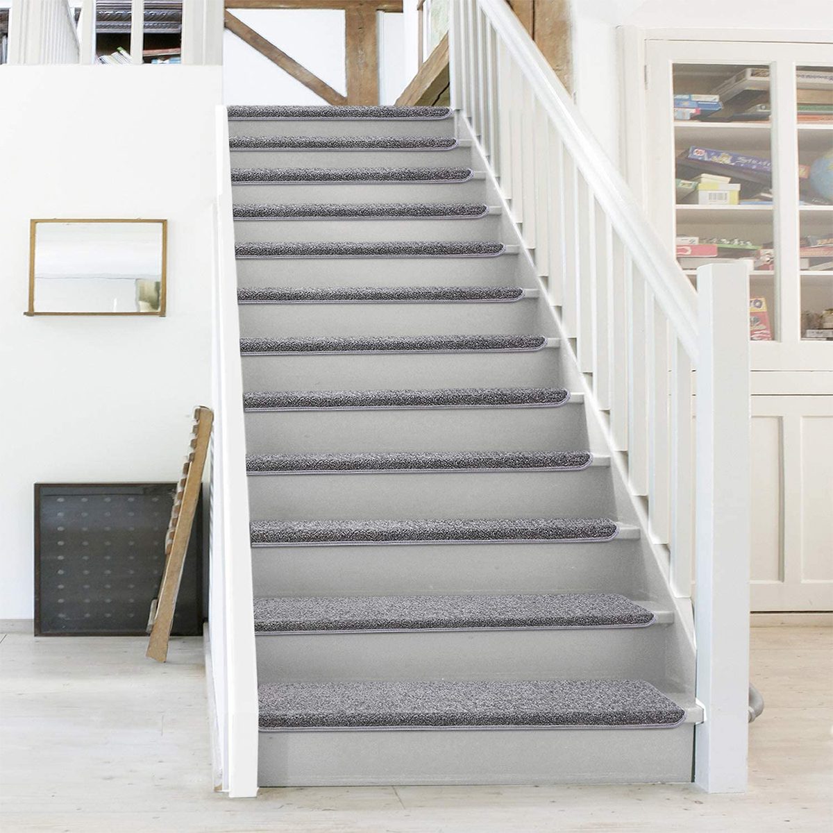 A staircase with grey carpeted treads ascends, flanked by a white railing, in a bright, minimalistic room featuring wooden accents and a mirror.