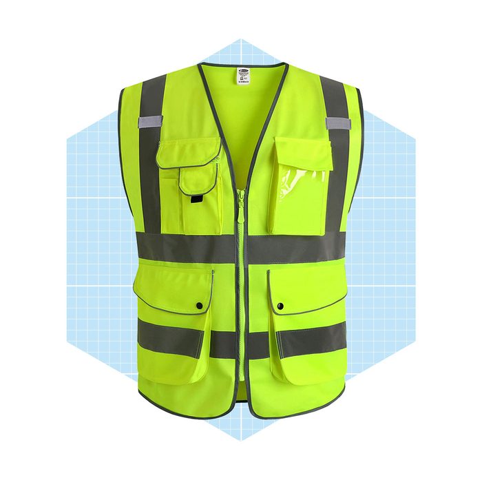 A bright yellow safety vest with reflective stripes hangs against a light blue grid background, featuring multiple pockets and a zip front closure.