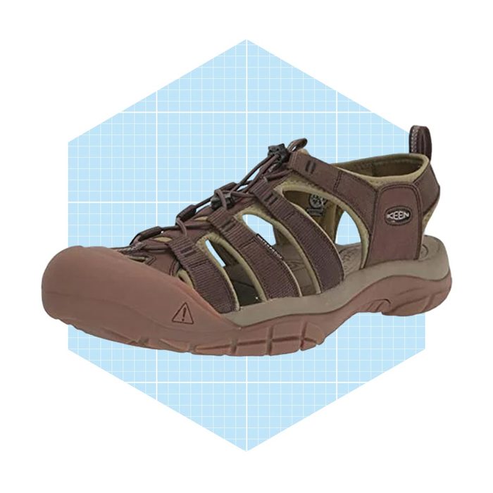 A brown sandal sits on a blue grid background, displaying its open design, adjustable straps, and rubber sole, ideal for outdoor activities.